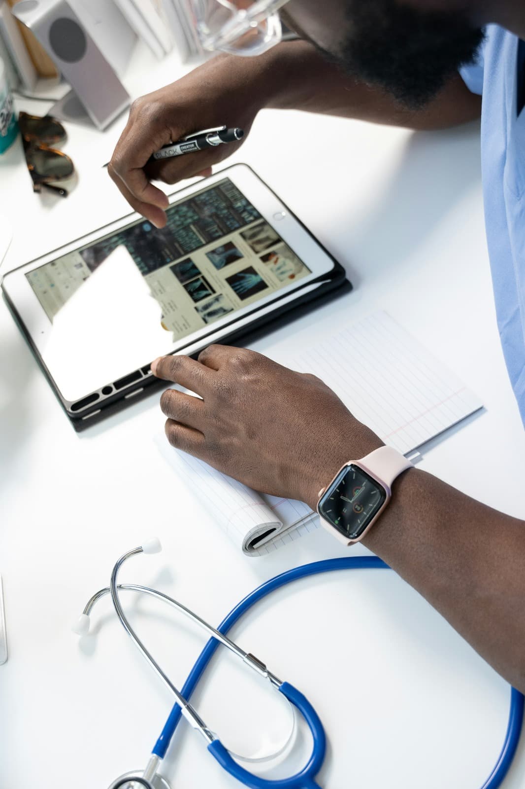 A clinician reviewing records on a tablet, with a stethoscope and notes on the desk